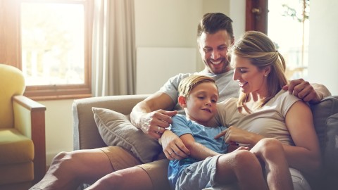 Mann und Frau entspannen mit einem Kind auf dem Schoß auf dem Sofa in einem hellen Zimmer.