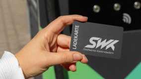 Hand hält SWK Ladekarte vor Ladestation für Elektrofahrzeuge von Stadtwerke Kaiserslautern.