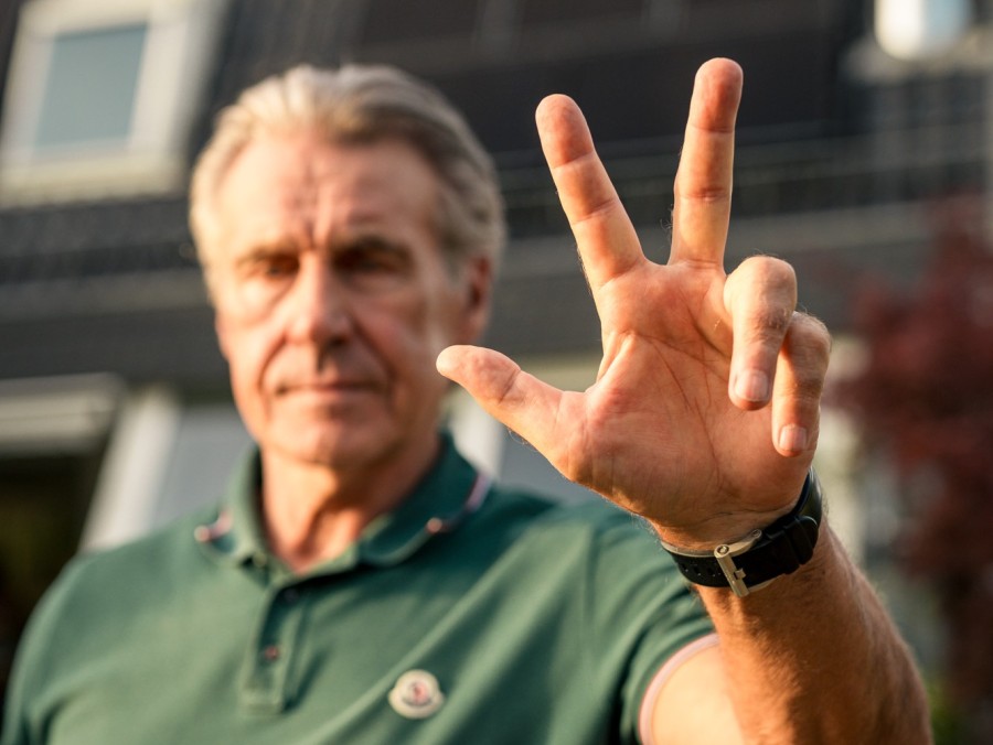 Gerry Ehrmann streckt Hand mit drei ausgestreckten Fingern nach vorne. Gesicht und Haus im Hintergrund sind unscharf.