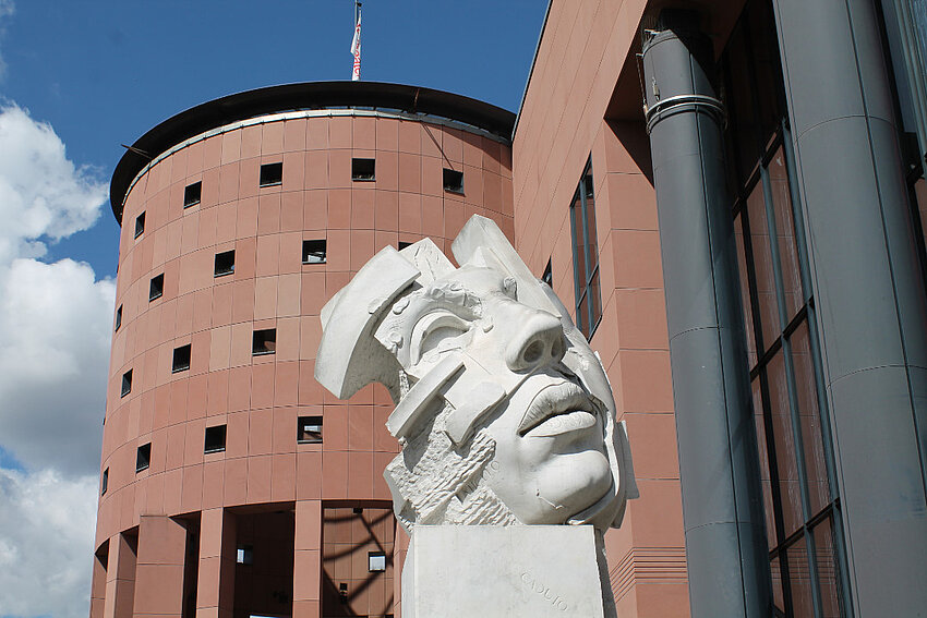 Gebäude Pfalztheater im nahen Seitenprofil mit Kunstfigur im Vordergrund.