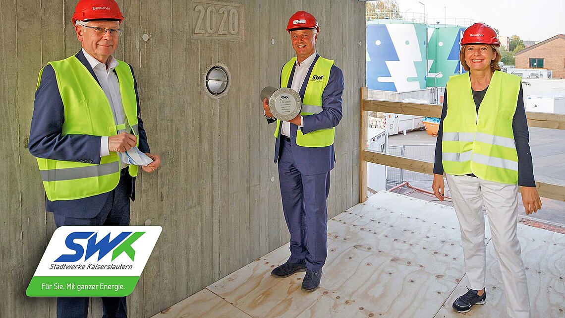Ehemaliger SWK-Vorstand hält eine Metallkapsel in seinen Händen weiterer SWK-Mitarbeiter und Malu Dreyer neben ihm