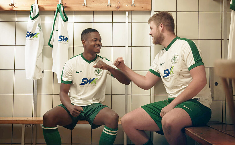 Spieler des Vereins F.C.Phonix Otterbach sitzen auf Bank in Trikot mit SWK darauf bedruckt geben sich die Faust 