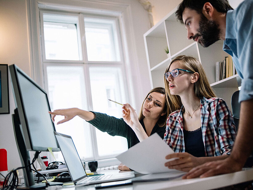 Personen im Büro schauen auf Monitor und zeigen darauf