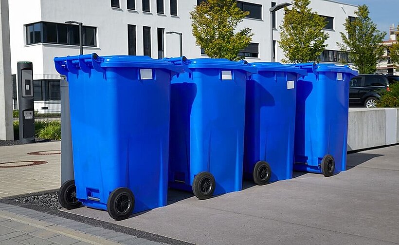 Blaue Mülltonnen vor Gebäuden stehen in einer Reihe