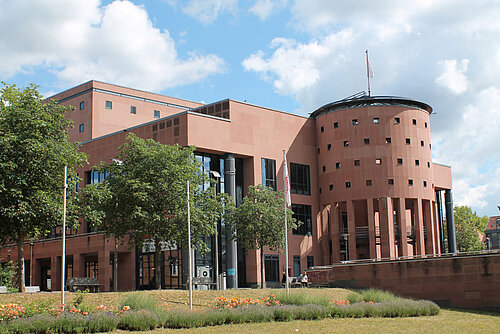 Gebäude Pfalztheater im Seitenprofil mit Bäumen und Wiese davor. 