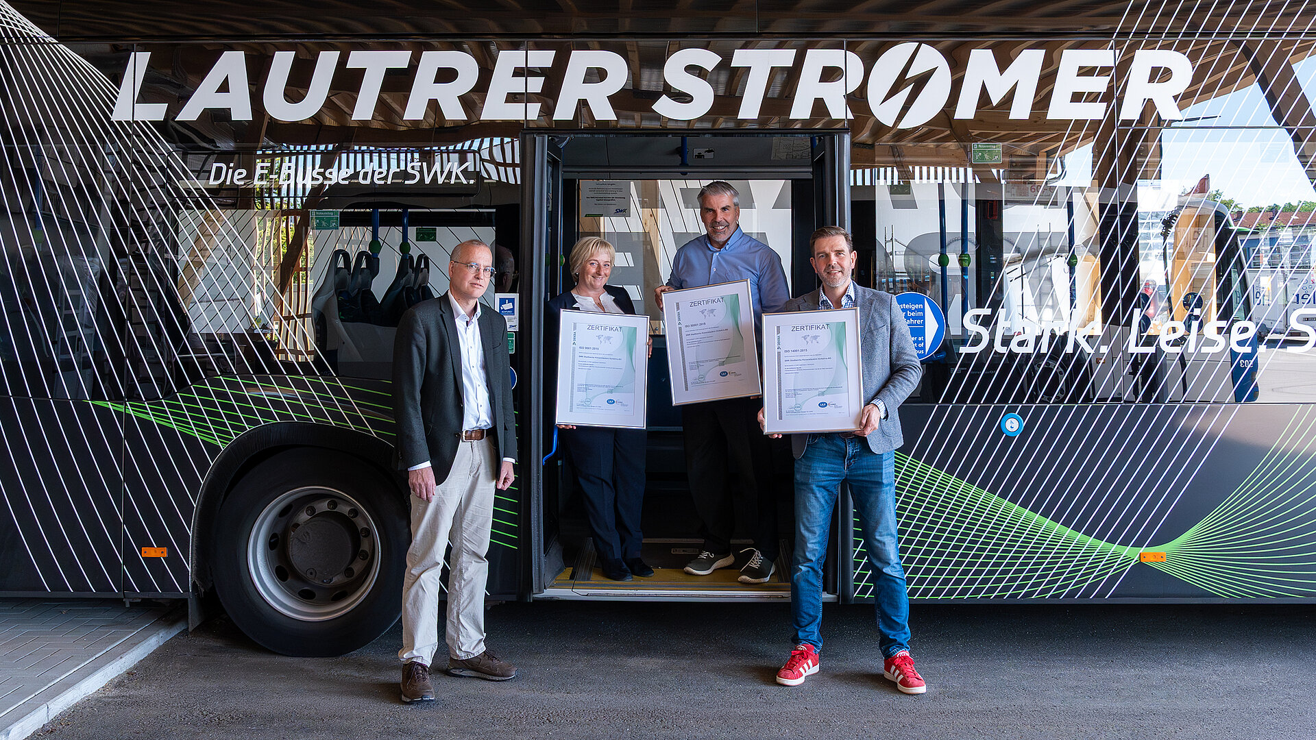 Vier Personen stehen vor und in der Tür eines Busses. Drei von ihnen halten Bilderrahmen mit den Zertifikaten in der Hand. 