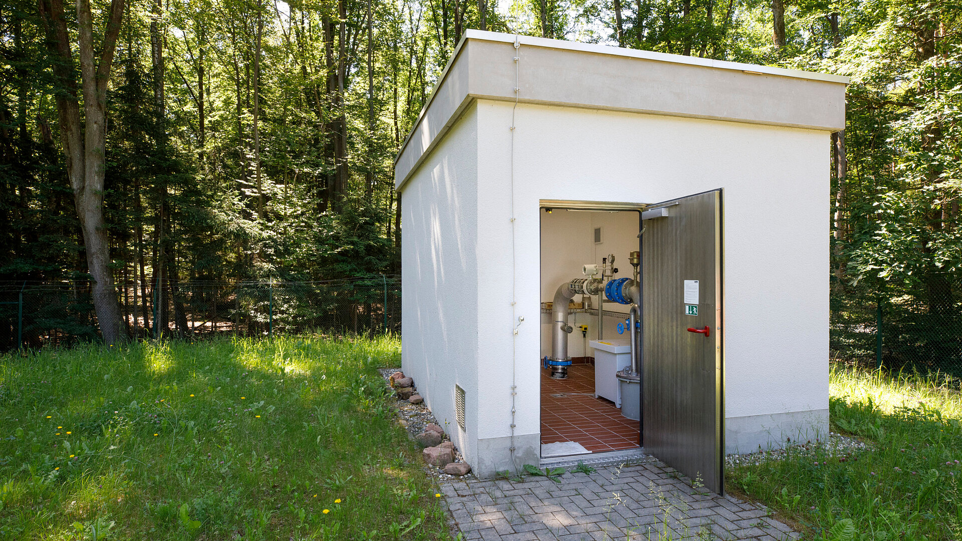 Technikgebäude zur Wasserversorgung im Wald mit offener Tür.