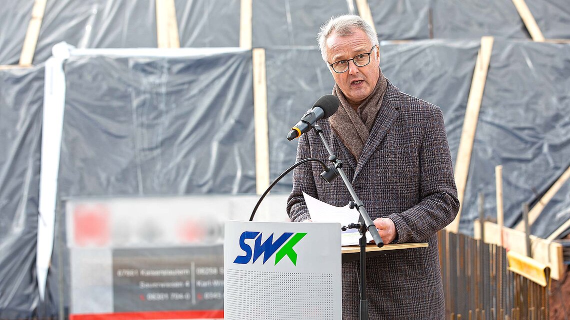 Mann spricht vor Baustelle am Mikrofon
