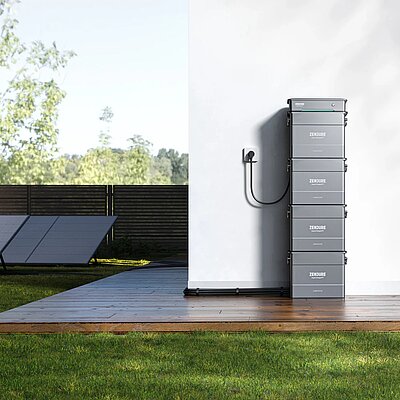 PV-Module im Garten und Batteriespeicher an Hauswand.