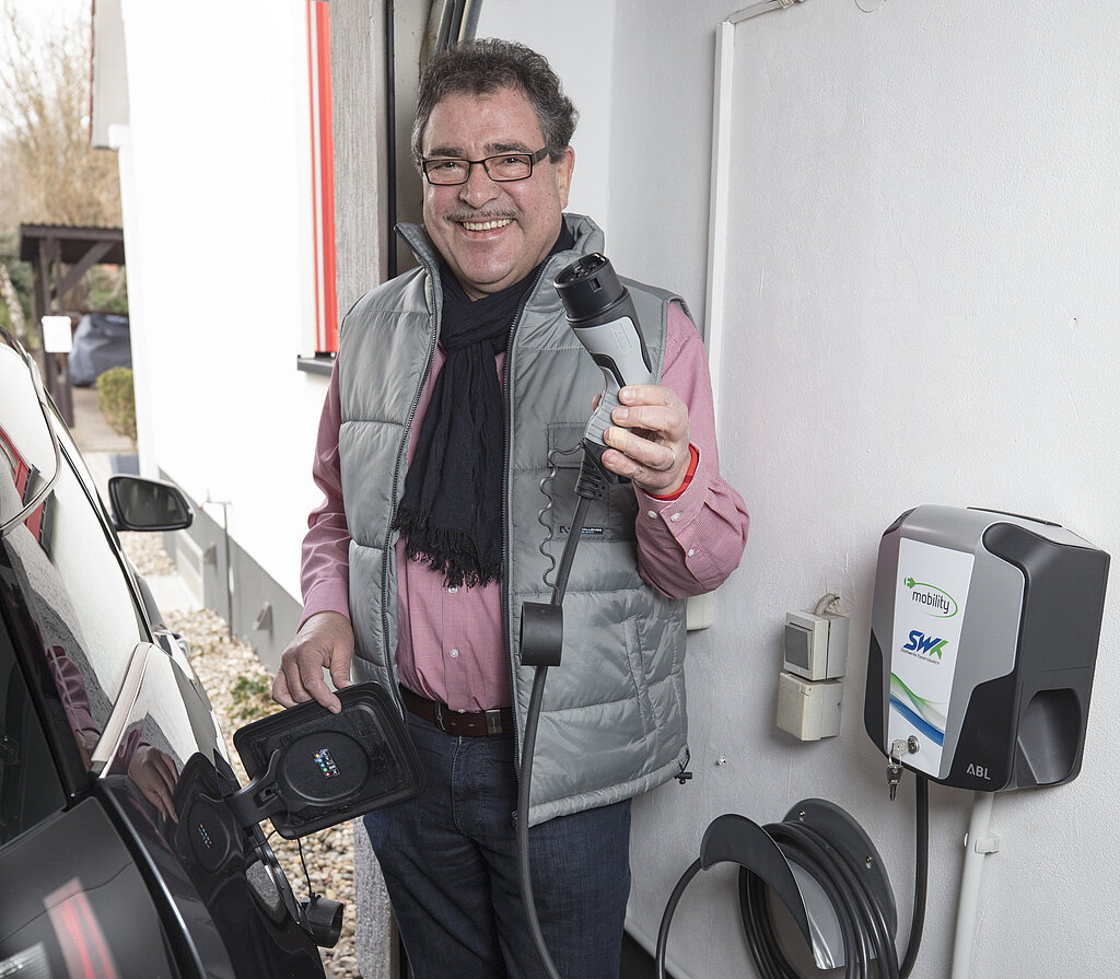 Mann an schwarzen BMW i3 hält Ladestecker von SWK-Wallbox in der Hand