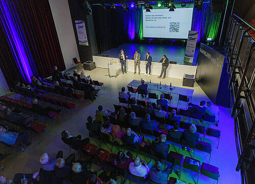 Saal mit Bühne und Publikum von oben.