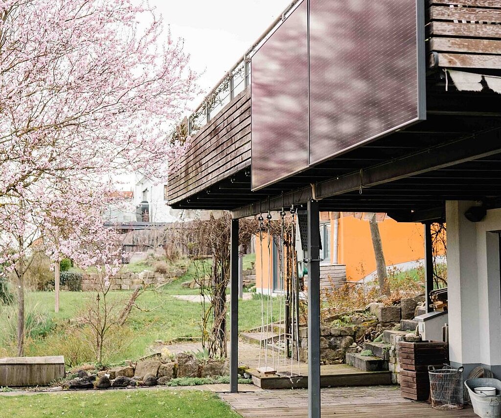 Solarmodule an einem Balkon, der über eine Terasse ragt. 
