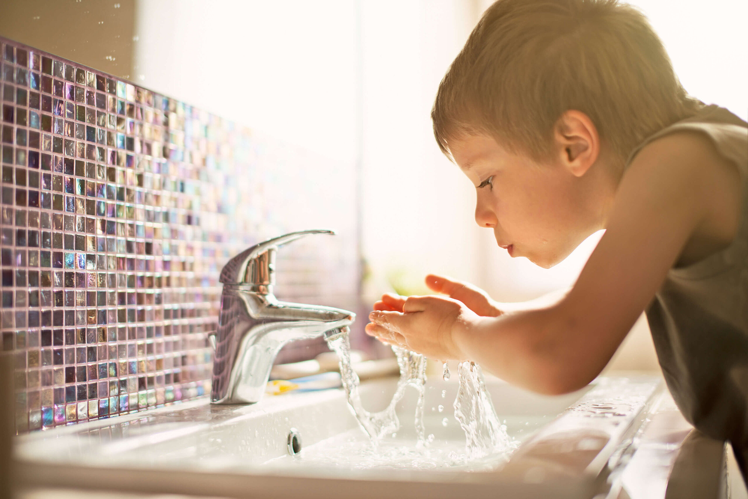 Junge am Waschbecken der Wasser aus seiner Hand trinkt
