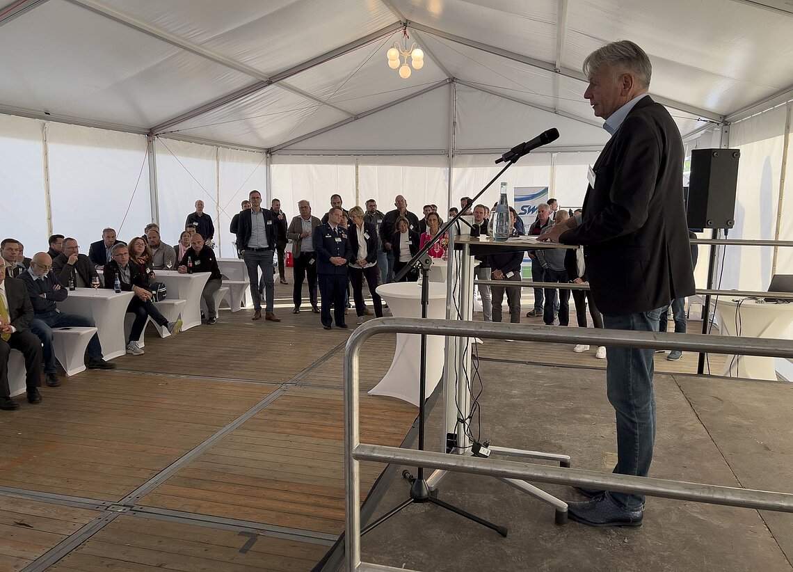 SWK-Mitarbeiter hält eine Rede auf einer Bühne vor weiteren Mitarbeitern