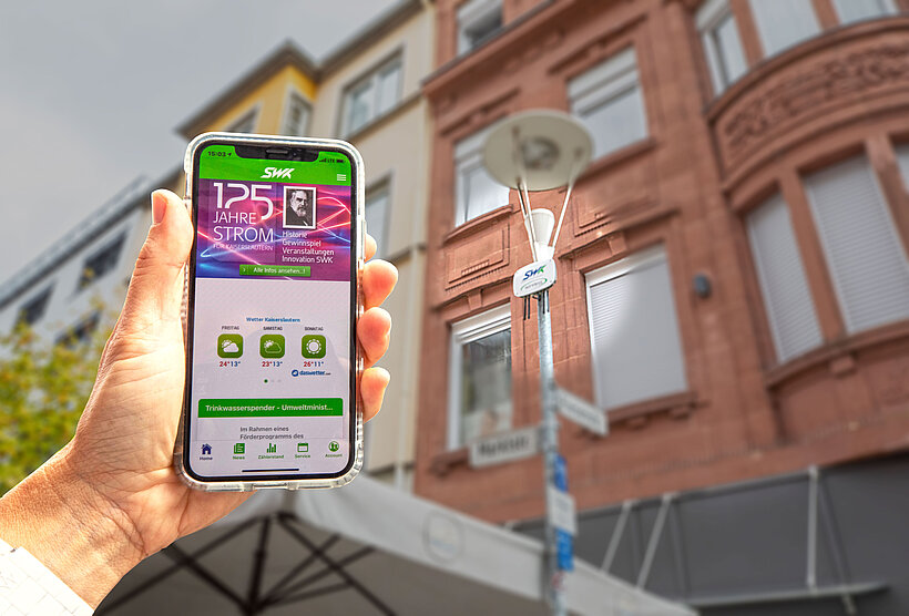 Person hält Handy mit SWK-App in seiner Hand und zeigt auf Laterne mit SWK City-Wlan 