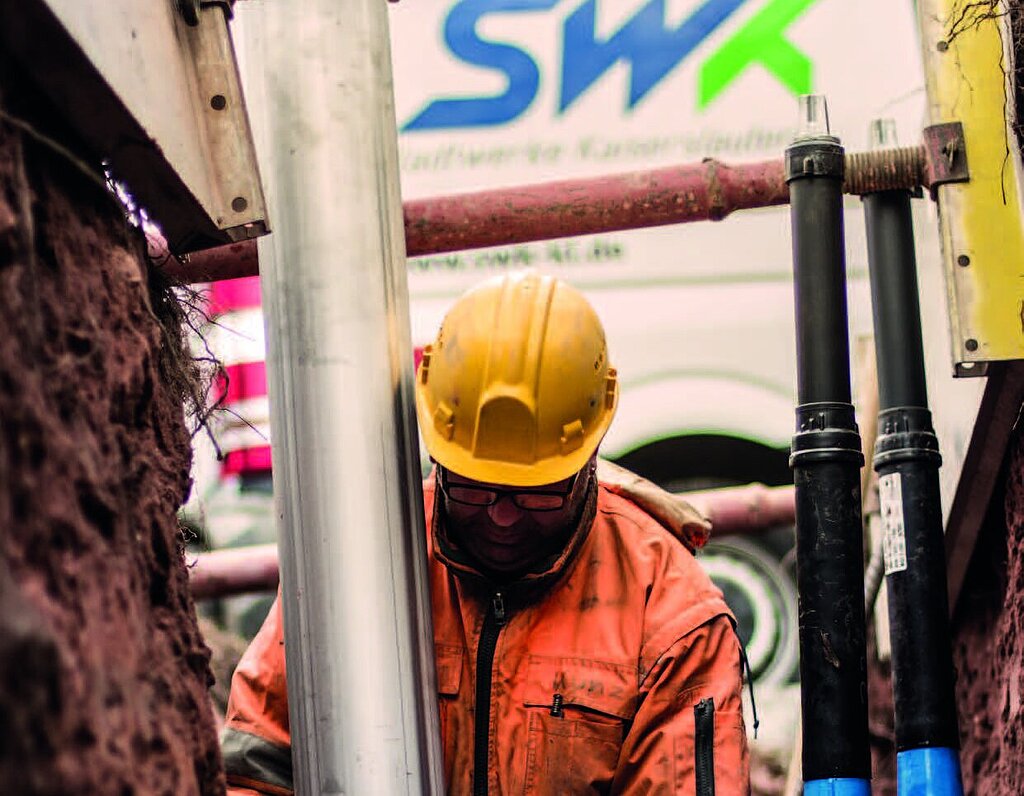 Mann arbeitet an einem Rohr an Baustelle, im Hintergrund SWK-Transporter