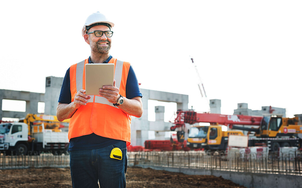 Mann mit Schutzhelm, Warnweste auf Baustelle mit Tablet